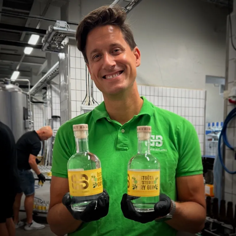 Alexander Åkerberg håller upp två flaskor gin i produktionen på Bränneribolaget